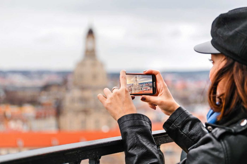 Eine junge Frau nimmt mit dem Smartphone ein Foto der Dresdner Frauenkirche auf.